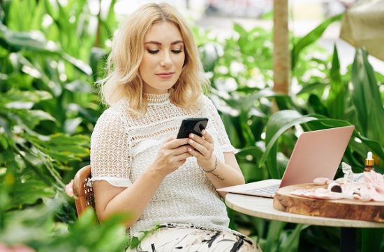 Blond charming Icelandic woman sitting using her smartphone and laptop