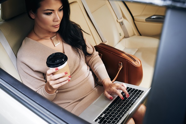 Young charming serious Thai woman sitting in her car with a cup of coffee working alone