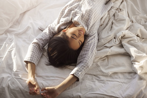 Charming young Japanese girl stretching in her bed after waking up in the morning