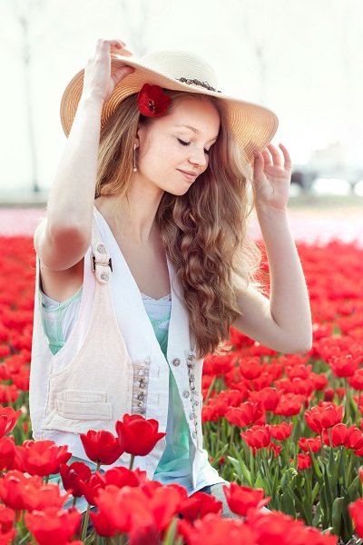 Beautiful smiling Dutch woman sitting on a field of red tulips touching the hat with her fingers