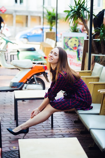 Smiling attractive Spanish female wearing a checkered dress sitting on a chair