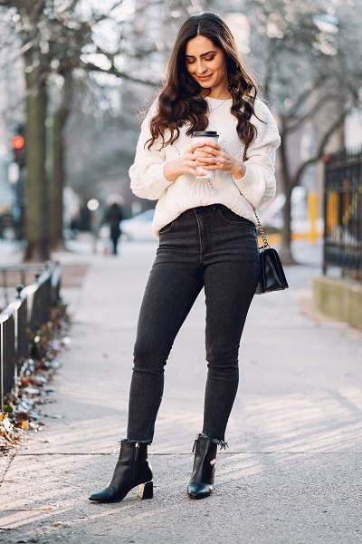 Cute brunette Serbian lady standing on a sidewalk with a cup of fresh coffee looking down