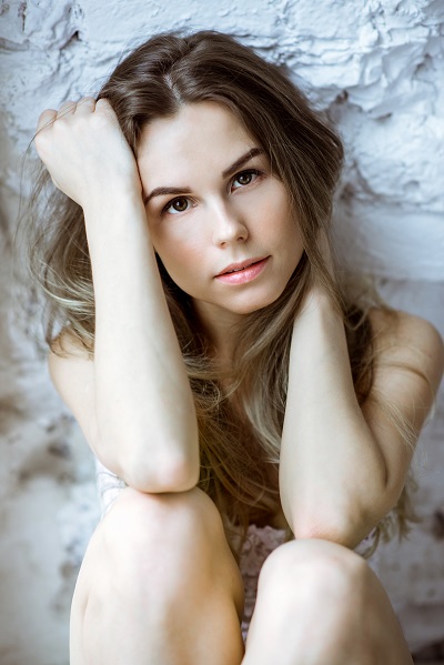 Cute young attractive Danish girl sitting by the white wall looking directly in the camera