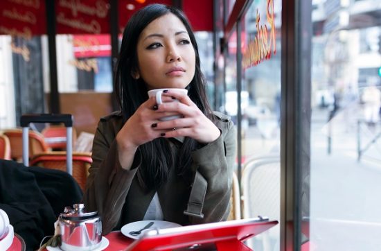 Young serious South Korean girl dreamily looking sideways with a cup of tea