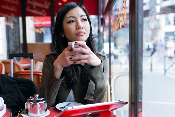 Young serious South Korean girl dreamily looking sideways with a cup of tea