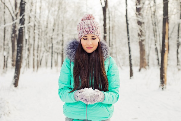 Young smiling brunette Swedish woman standing in a winter forest playing with snow