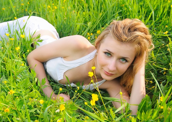 Charming Latvian woman lying in green grass in a field during the summer