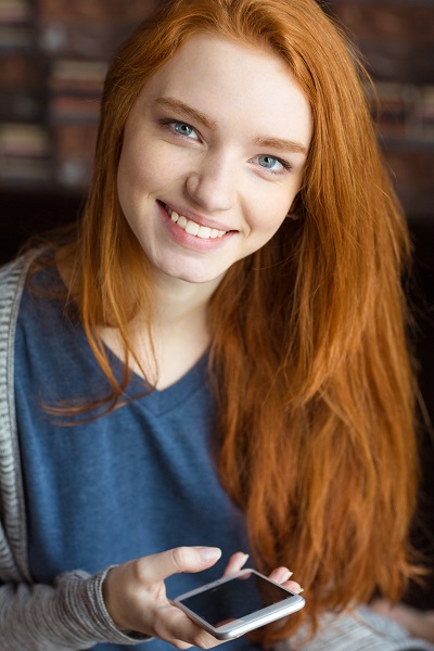 Smiling red-haired Irish girl holding her phone looking directly in the camera