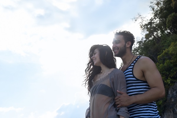 Young smiling Costa Rican woman standing with her man looking sideways together