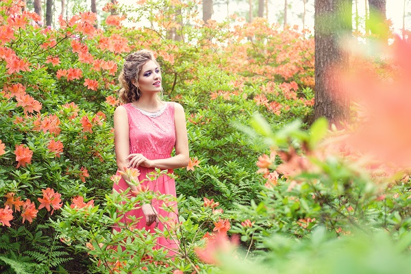 Curvy blonde Greek woman wearing a pink dress standing in a green garden full of flowers